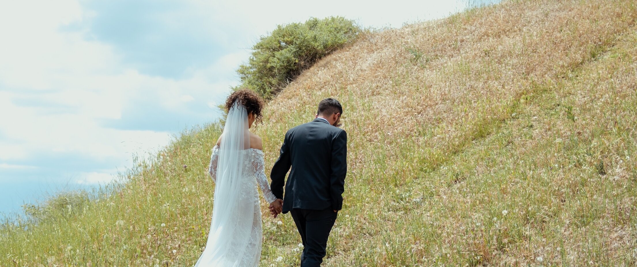 Bride and groom holding hands while walking up a grassy mountain hillside