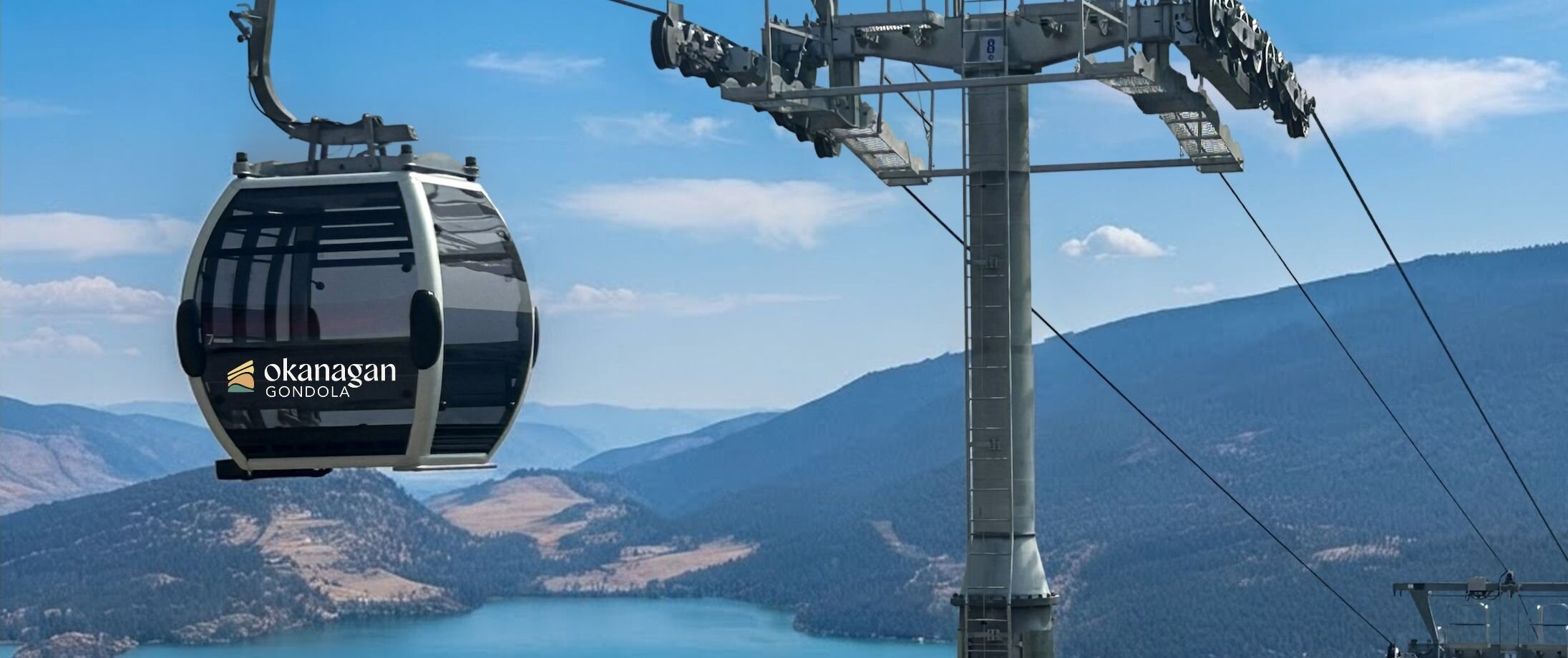 Modern CWA gondola cabin passing a steel lift tower with panoramic views of Kalamalka Lake and surrounding mountains at the Okanagan Gondola