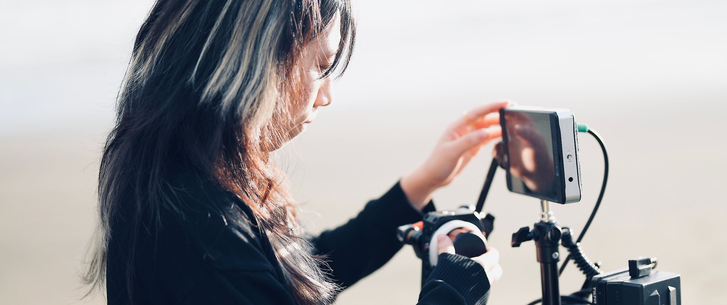 Female videographer adjusting a professional camera setup and monitor stand outdoors.