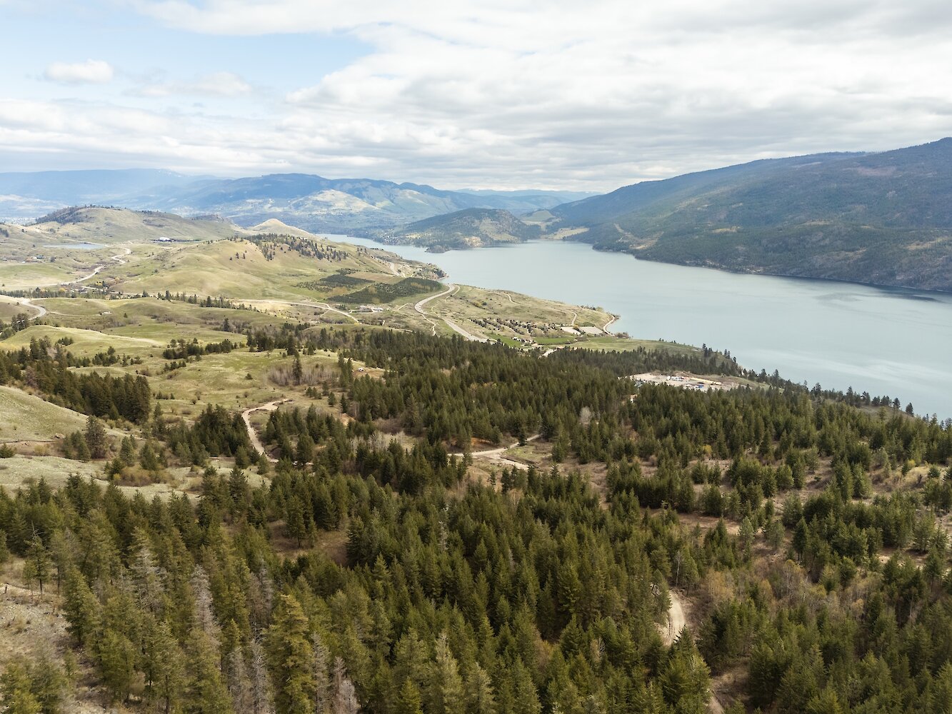 Aerial drone view showing pine forest trails, rolling hills, and Kalamalka Lake at the Okanagan Gondola