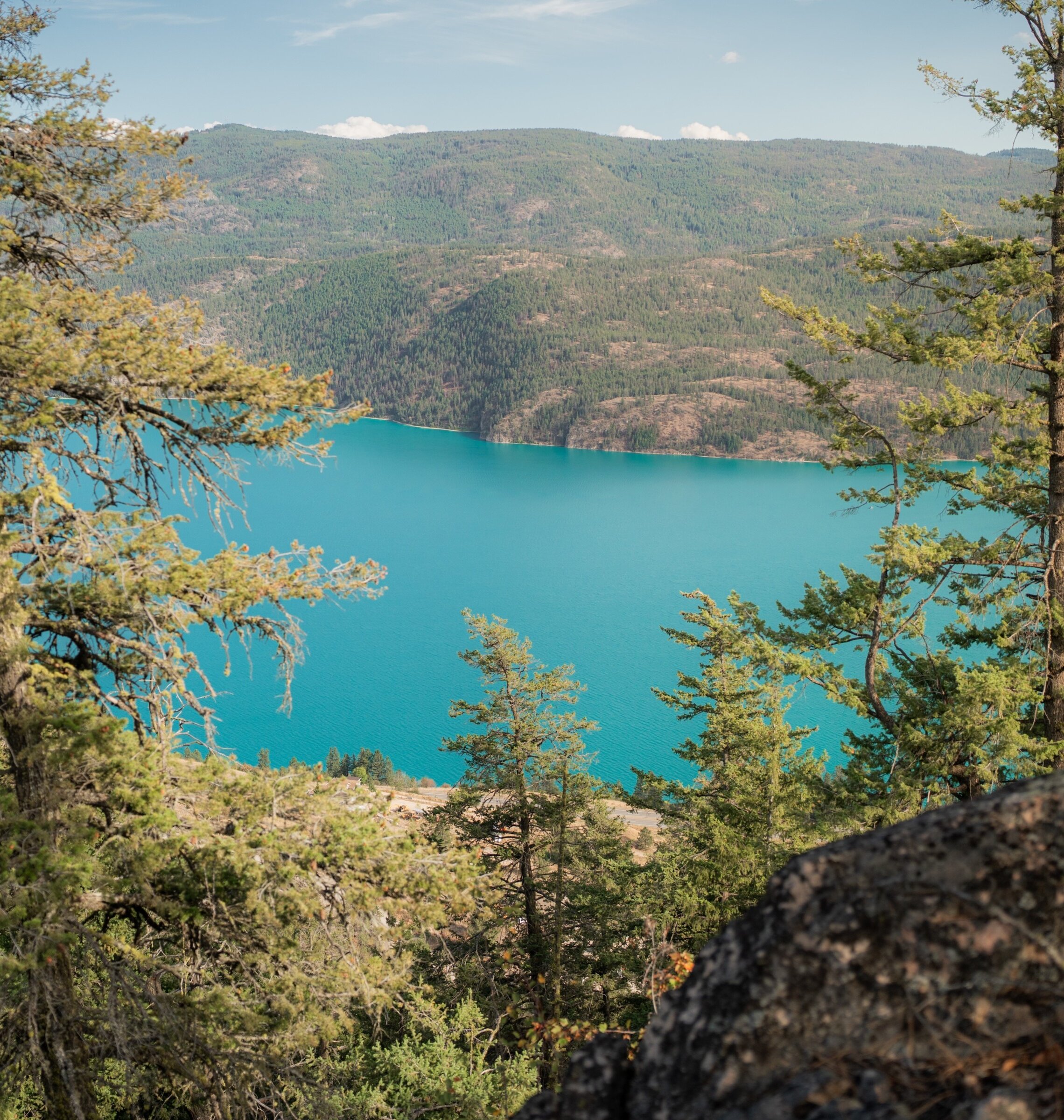 View from a rocky mountain lookout framed by pine trees overlooking the turquoise waters of Kalamalka Lake at the Okanagan Gondola