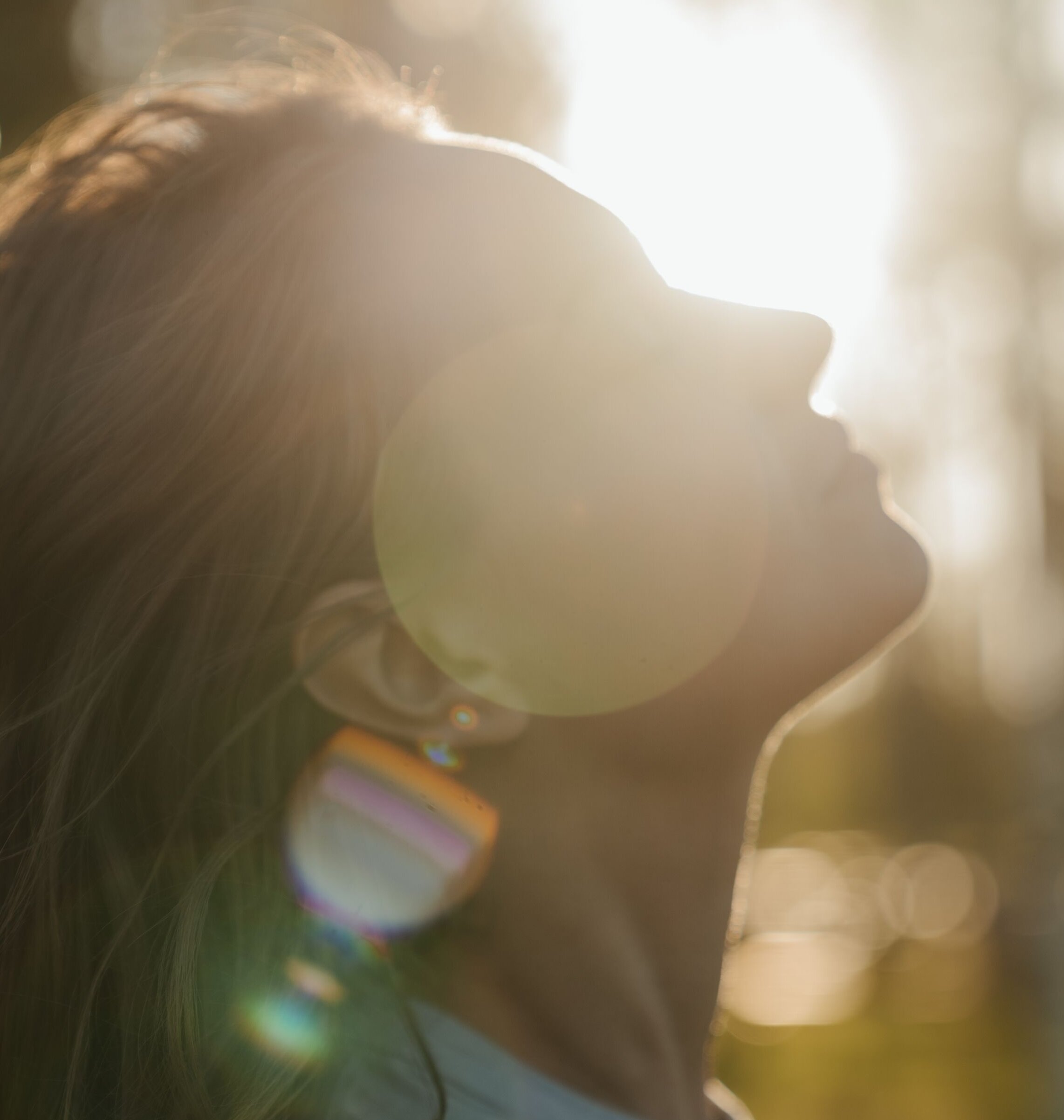Profile of a woman tilting her head back with eyes closed, enjoying warm sunlight and lens flare outdoors